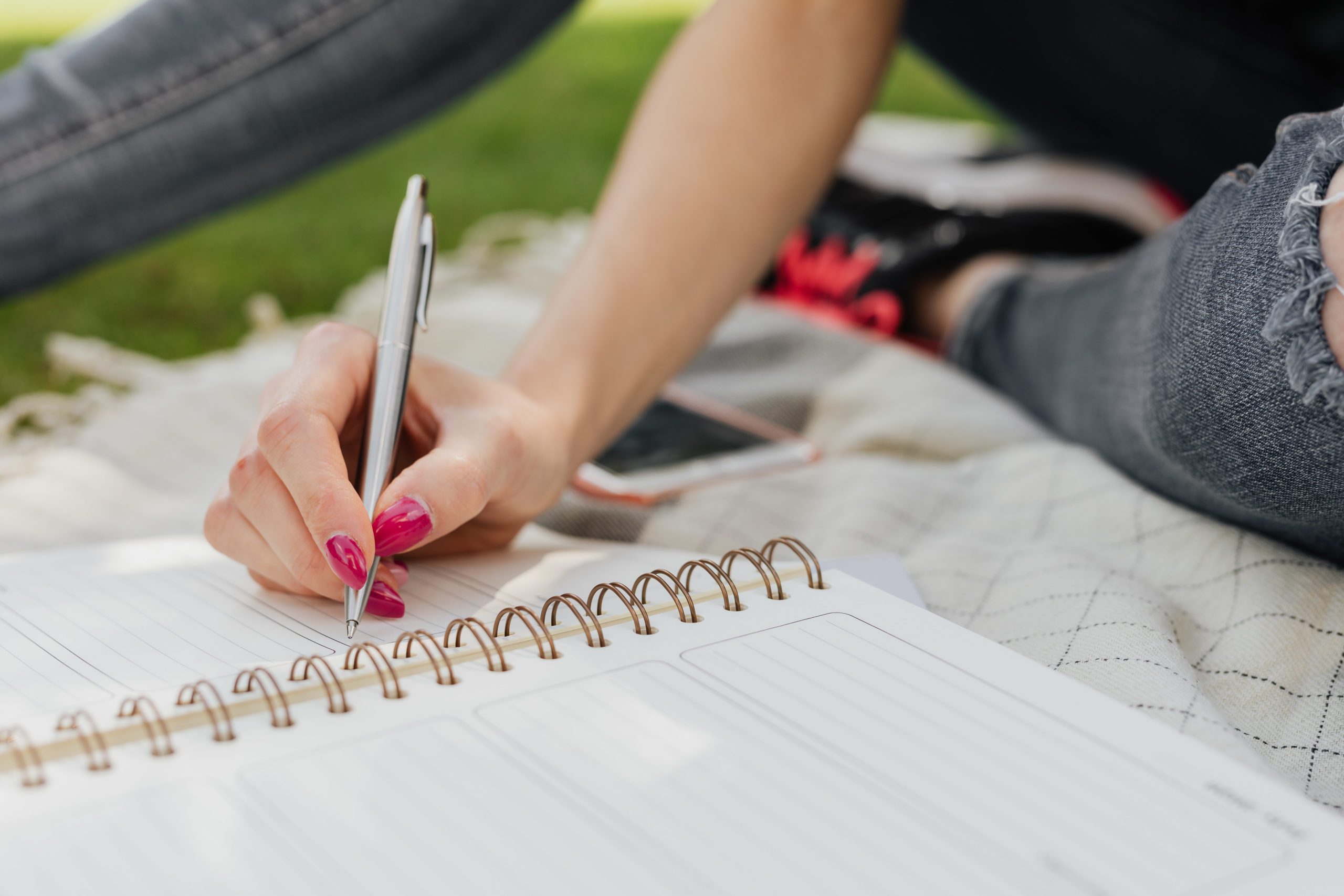 crop-female-noting-down-daily-plans-in-notebook-in-park-4497758